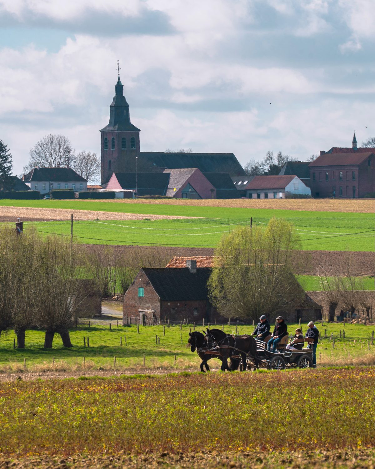 De kerktoren van Huise boven de velden, met een menwagen